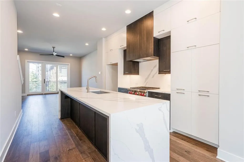 Kitchen featuring dark hardwood / wood-style floors, light stone counters, an island with sink, and ceiling fan