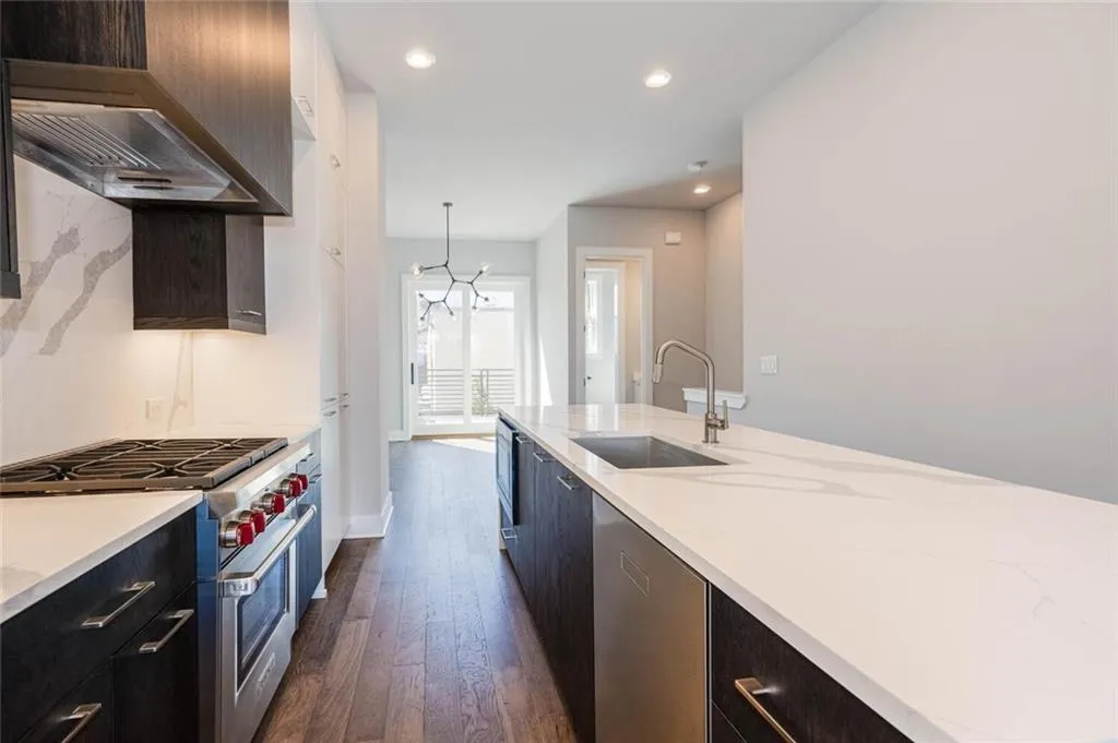 Kitchen with pendant lighting, wall chimney exhaust hood, appliances with stainless steel finishes, dark hardwood / wood-style floors, and sink