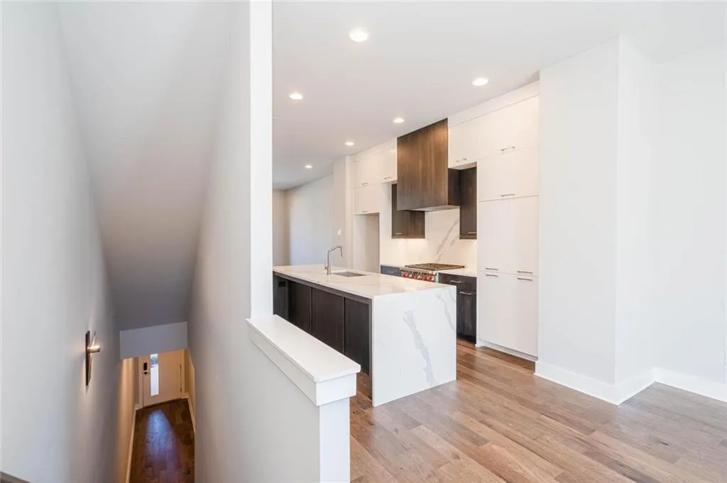 Kitchen featuring an island with sink, stainless steel gas stovetop, sink, light wood-type flooring, and white cabinetry