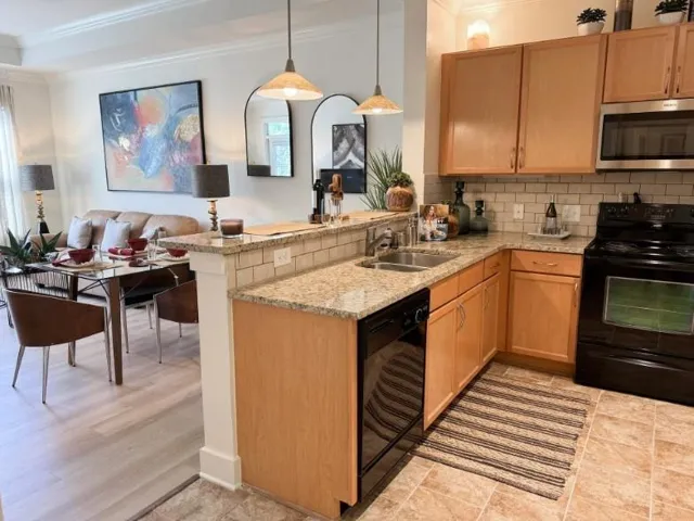 Kitchen with crown molding, black appliances, light stone countertops, tasteful backsplash, and a peninsula
