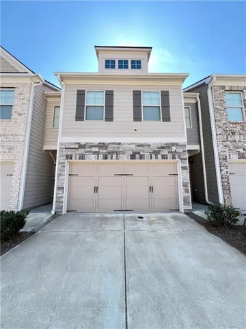 Two-story townhouse featuring a two-car garage with decorative hardware, stone accents, and a distinctive cupola