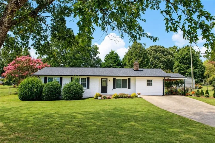 White exterior with black shutters, a dark shingle roof, a brick chimney, and a paved driveway