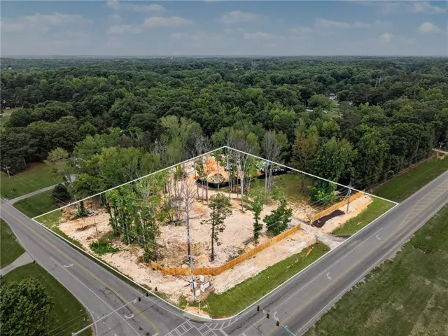Expansive corner parcel featuring mature trees, a partially cleared building area, and perimeter fencing