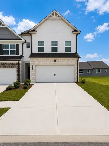 Two-story exterior featuring white brick and shake siding, an attached two-car garage, concrete driveway, and foundational landscaping