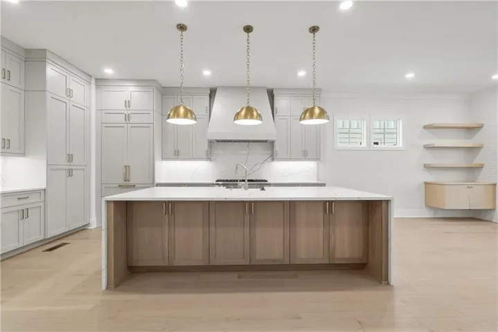 *Picture is of same floorplan but not of actual home. White oak wood-finish flooring, custom light gray cabinetry, central island with waterfall edge countertop, built-in cooktop, and brass-finish pendant lighting