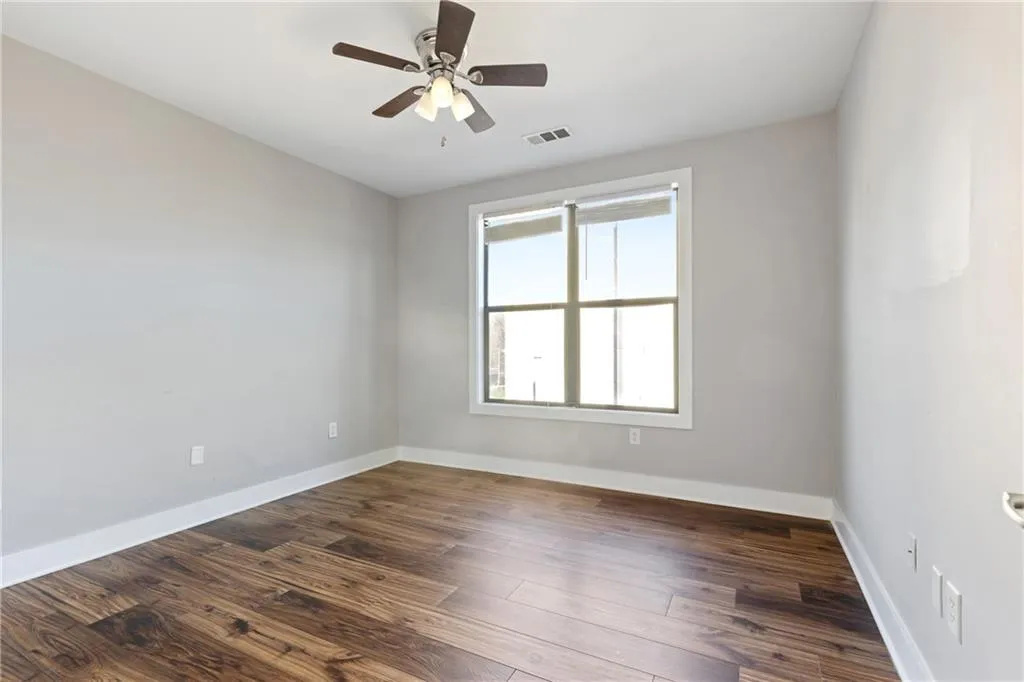 Unfurnished room featuring dark wood-style floors, visible vents, baseboards, and a ceiling fan