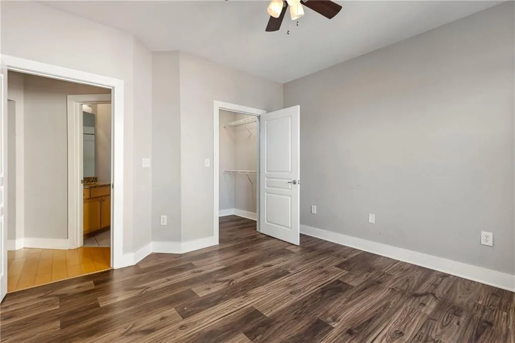 Unfurnished bedroom featuring ceiling fan, dark wood-type flooring, baseboards, a spacious closet, and a closet