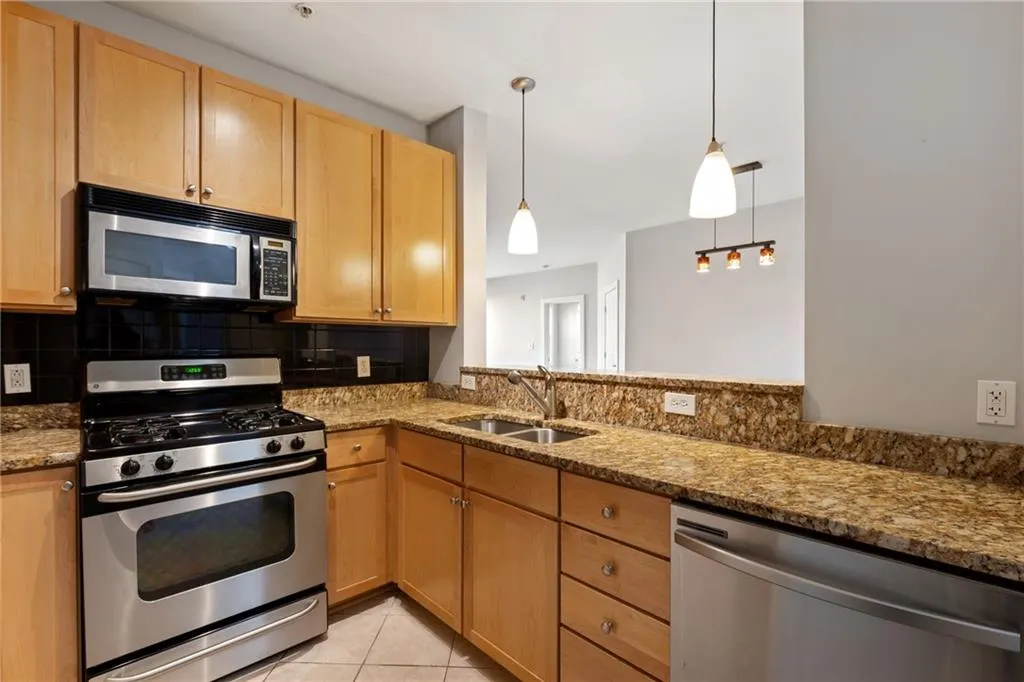 Kitchen featuring light tile patterned floors, tasteful backsplash, appliances with stainless steel finishes, stone counters, and a sink