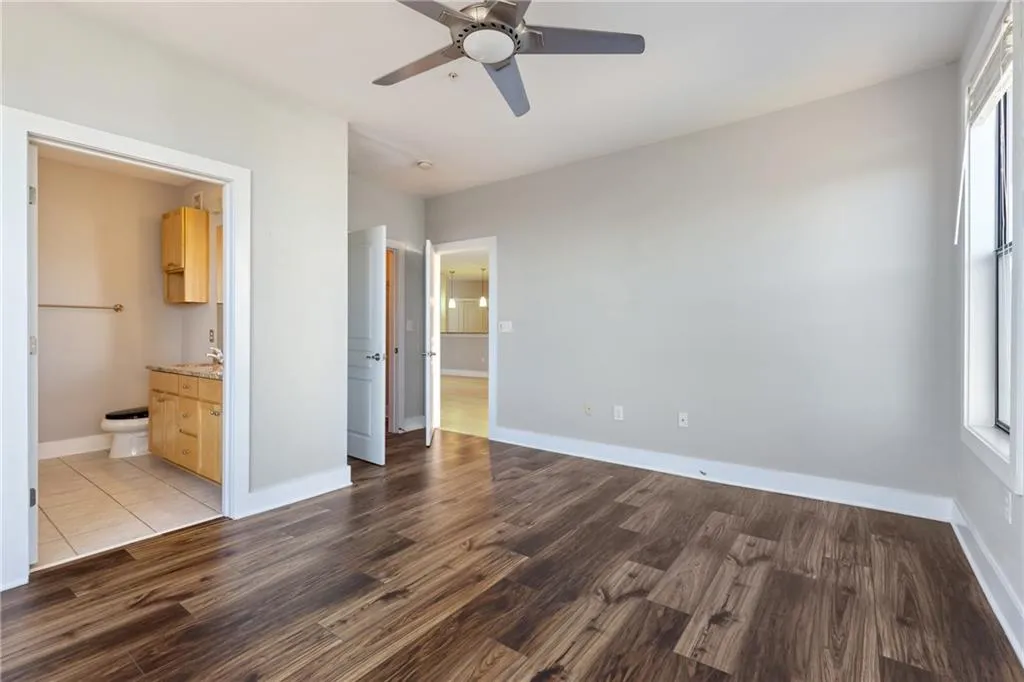 Unfurnished bedroom with a ceiling fan, connected bathroom, baseboards, and wood finished floors
