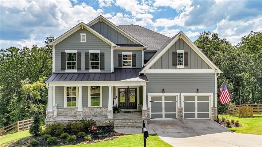Two-story residence featuring a gray exterior with stone accents, a covered front porch, a metal awning, and a two-car garage
