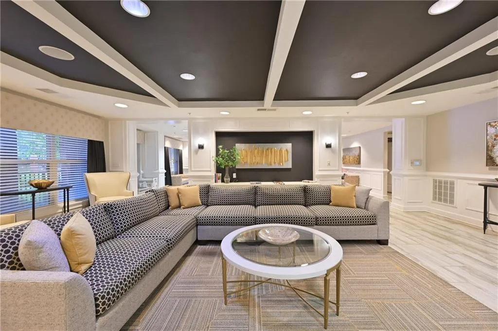 Living room with a decorative wall, beamed ceiling, light wood-type flooring, recessed lighting, and wainscoting