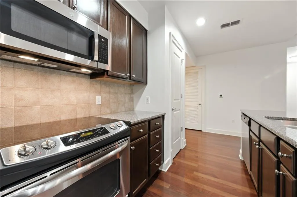 Kitchen with dark brown cabinets, stainless steel appliances, dark wood-type flooring, light stone countertops, and recessed lighting