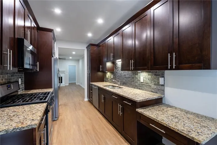 Galley kitchen featuring rich wood cabinetry, granite countertops, stainless steel appliances, and a tiled backsplash