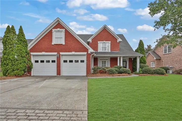 Brick exterior with a covered porch, white columns, two-car garage, and a concrete driveway