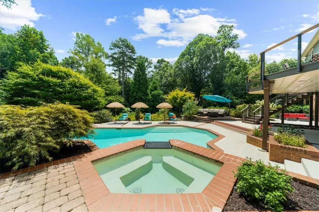 View of pool with stairway, a patio area, a pool with connected hot tub, and view of scattered trees