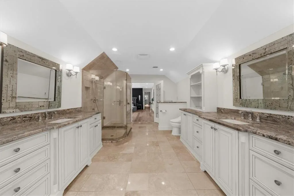 Bathroom with a stall shower, two vanities, vaulted ceiling, and recessed lighting
