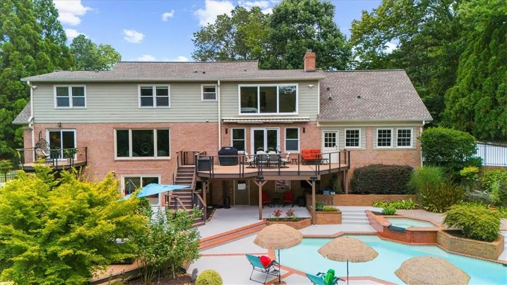 Back of property featuring an in-ground hot tub, a deck, a chimney, stairs, and a patio