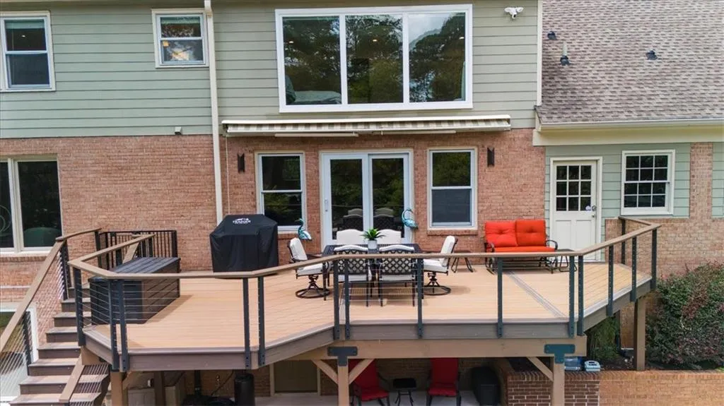 Back of house with a wooden deck, outdoor dining space, brick siding, stairway, and roof with shingles