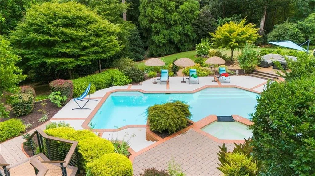 View of pool with a patio, a pool with connected hot tub, and a view of trees