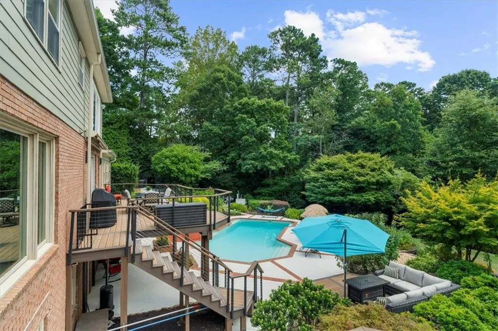 Swimming pool with stairway, a wooden deck, a patio, an outdoor living space, and a grill
