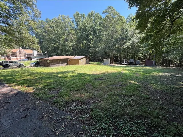 Expansive lot featuring a grassed area, mature trees, and a detached structure with a covered porch