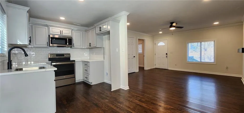 Kitchen featuring a sink, stainless steel appliances, crown molding, light countertops, and backsplash