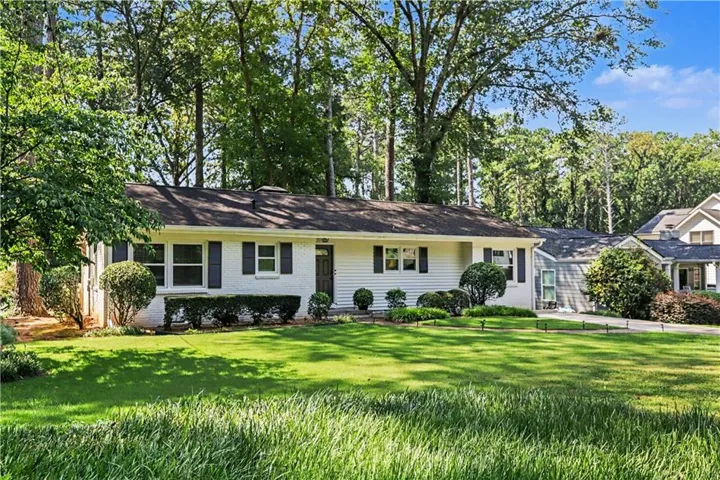 White brick exterior with dark shutters, front lawn with mature trees, and established landscaping