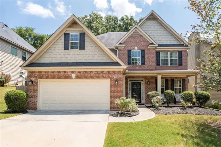 Traditional brick and siding exterior featuring a covered front porch with white columns, a two-car garage, and a concrete driveway