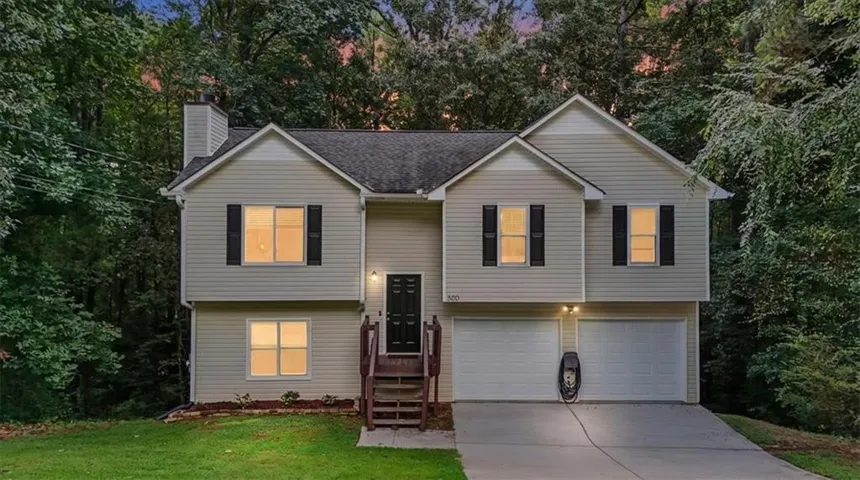 Split-level home featuring light-colored siding, dark shutters, a two-car garage, and an exterior EV charging station