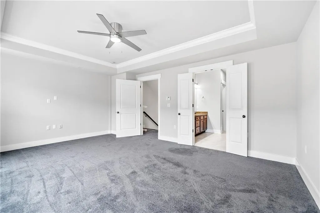 bedroom with connected bathroom, a raised ceiling, carpet flooring, a ceiling fan, and crown molding