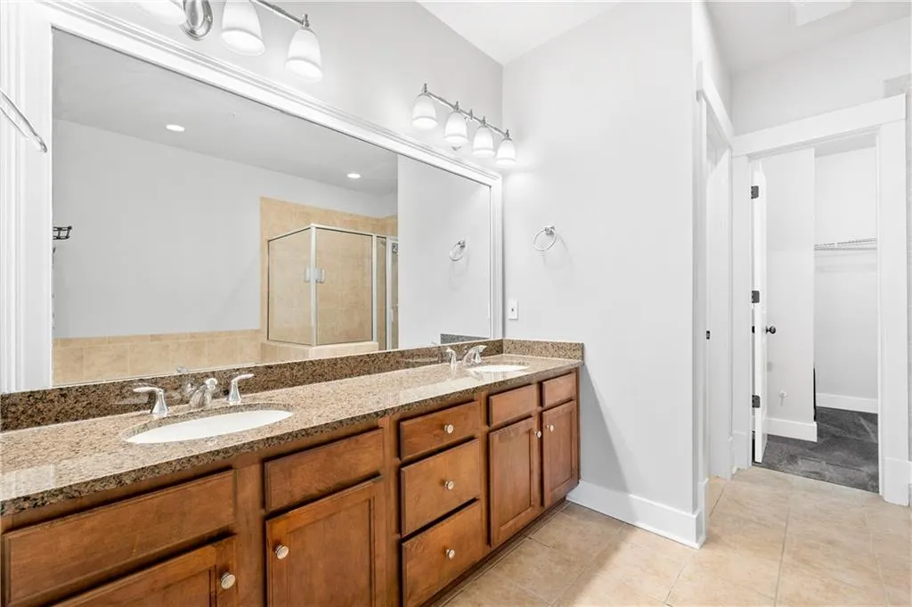 Full bath with double vanity, a spacious closet, a stall shower, and light tile patterned flooring