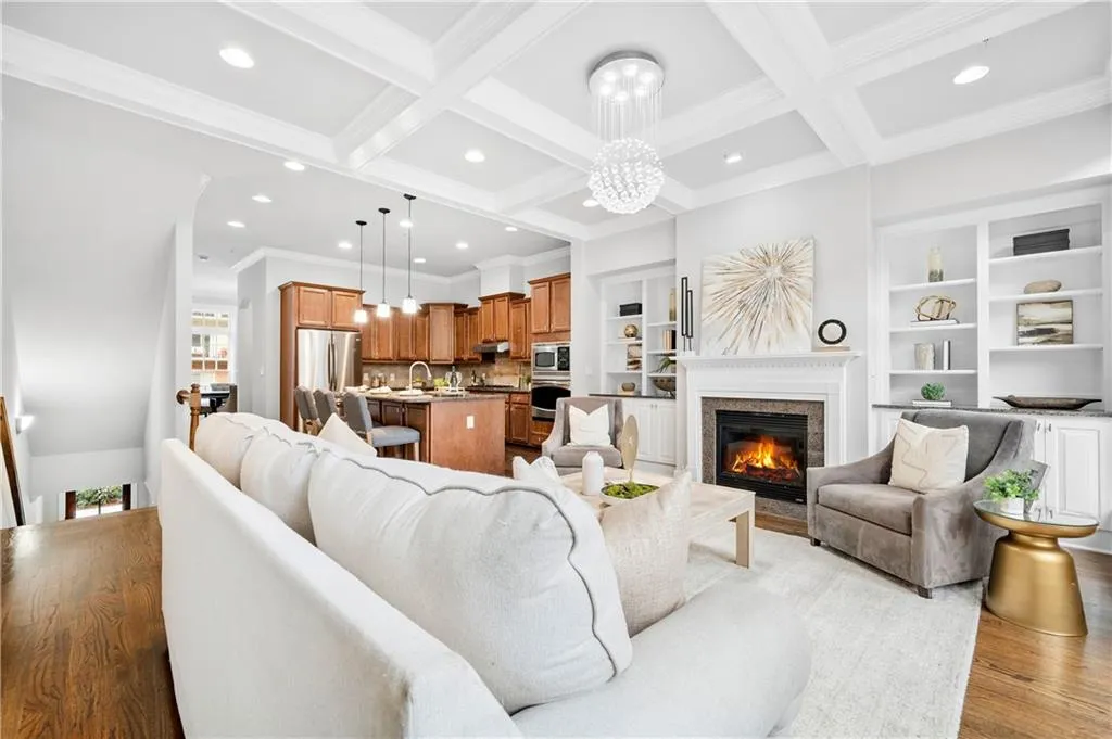 Living area featuring coffered ceiling, a premium fireplace, ornamental molding, hanging lights, and light wood-style flooring