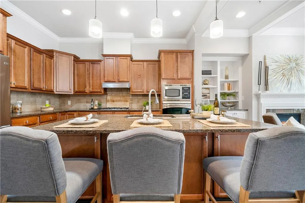 Kitchen with a breakfast bar, wood finish cabinetry, hanging light fixtures, dark stone countertops, and ornamental molding
