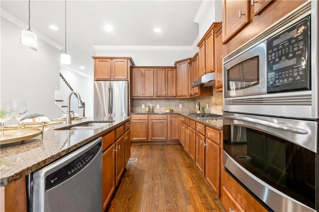 Kitchen featuring stainless steel appliances, wood finish cabinetry, pendant lighting, dark wood finished floors, and dark stone counters
