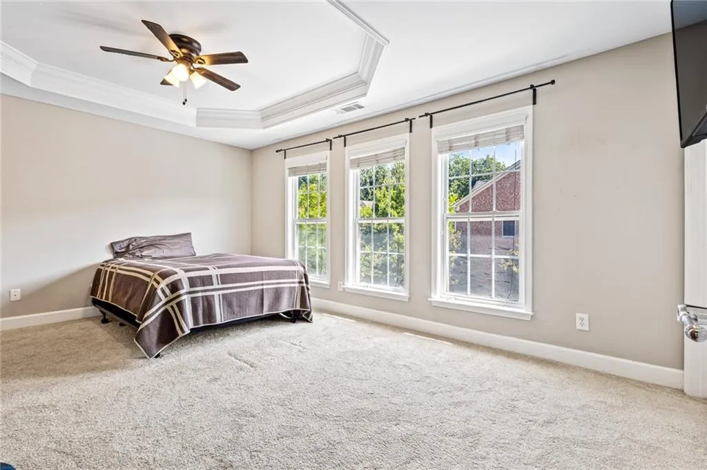 Carpeted bedroom with a tray ceiling, ornamental molding, and ceiling fan