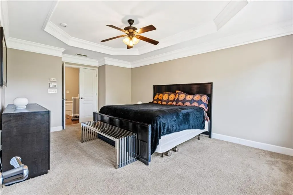 Bedroom featuring a tray ceiling, carpet, ornamental molding, and ceiling fan