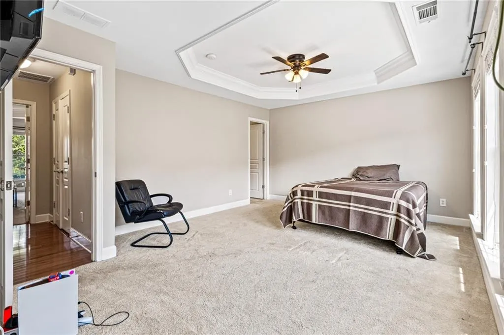 Carpeted bedroom with a raised ceiling, crown molding, and a ceiling fan