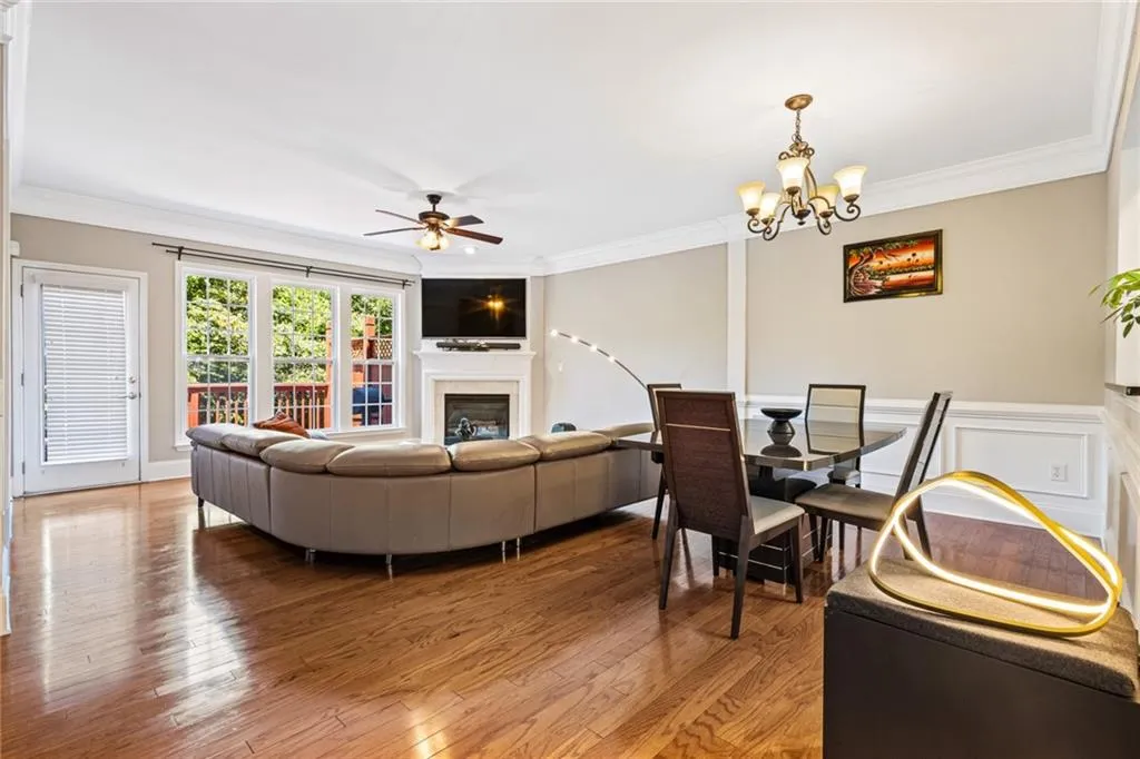 Living room with light wood finished floors, crown molding, ceiling fan, a glass covered fireplace, and a chandelier