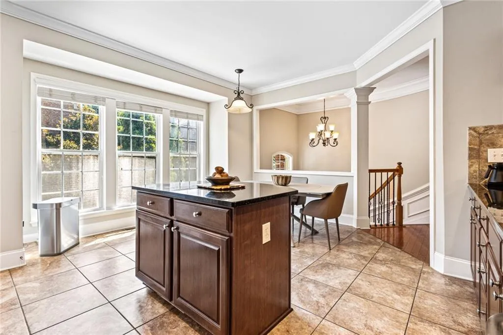 Kitchen featuring decorative light fixtures, ornamental molding, light tile patterned floors, dark brown cabinets, and a chandelier