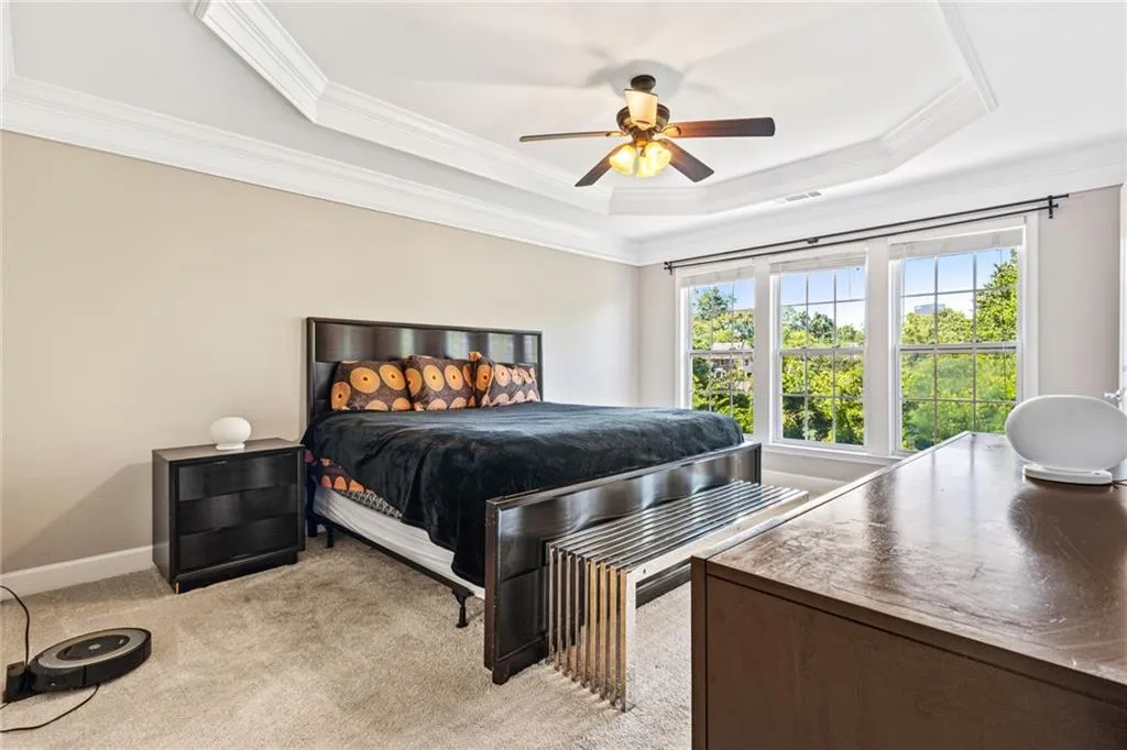 Bedroom with light carpet, crown molding, a raised ceiling, and ceiling fan