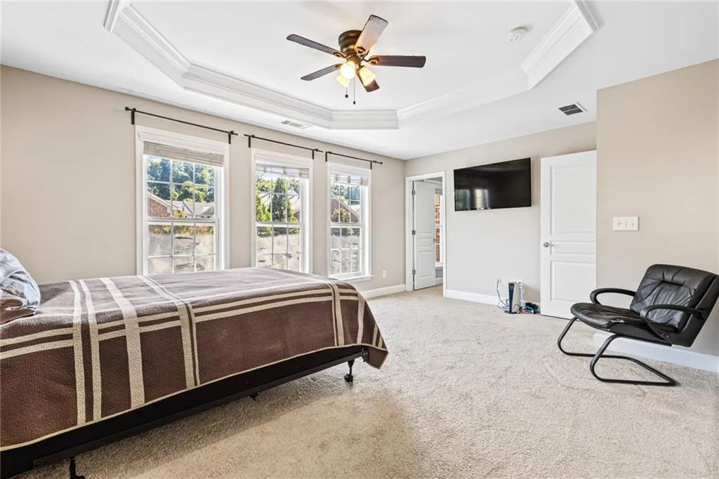 Bedroom featuring a raised ceiling, carpet flooring, ornamental molding, and ceiling fan