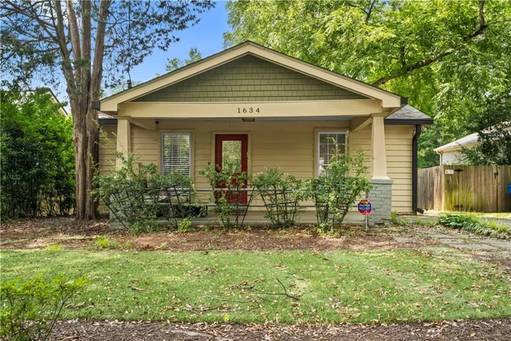 Charming bungalow facade featuring a covered front porch, a red entry door, and a decorative gable with green shake siding