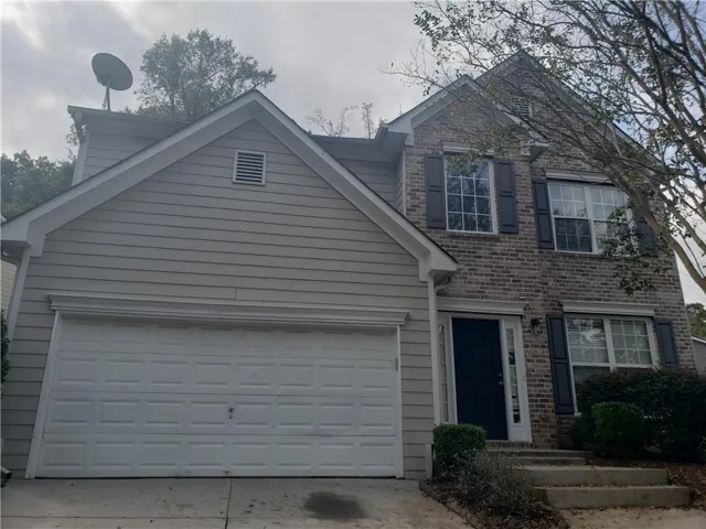Brick and siding exterior with a two-car garage, multiple windows with dark shutters, and a dark entry door