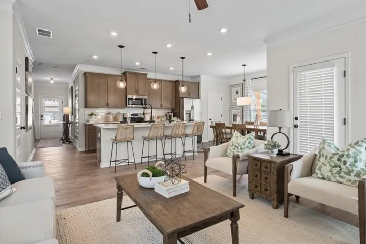Open-concept living space featuring wood-finish flooring, recessed lighting, a kitchen island with pendant lights, white subway tile backsplash, and stainless steel appliances