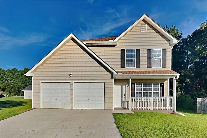 Two-story residence featuring light-colored siding, a covered front porch with white railing, and a two-car garage with white doors