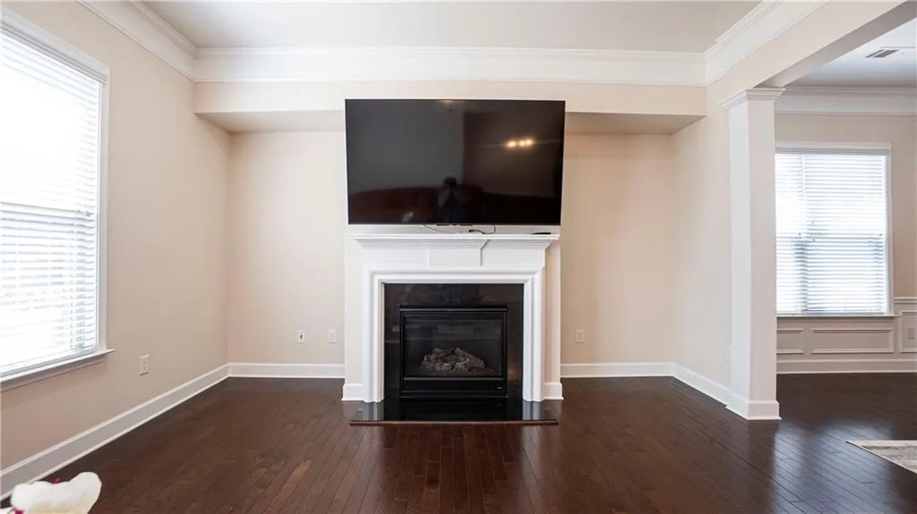 Unfurnished living room featuring dark wood-style floors, ornamental molding, and a glass covered fireplace