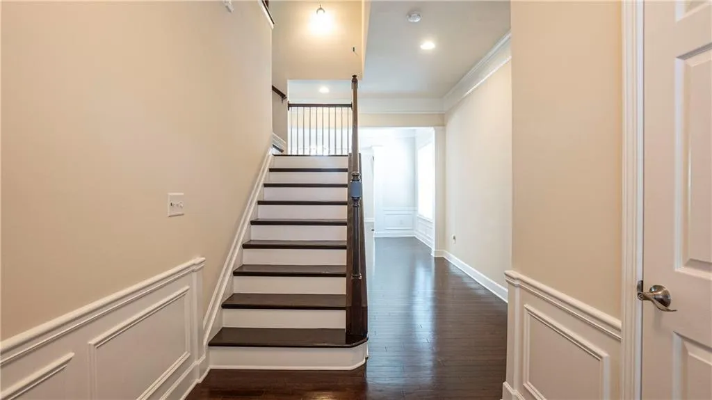 Stairs featuring crown molding, a decorative wall, wood finished floors, a wainscoted wall, and recessed lighting