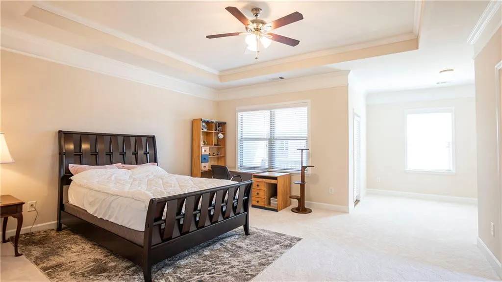 Bedroom featuring a tray ceiling, light carpet, crown molding, a ceiling fan, and a desk