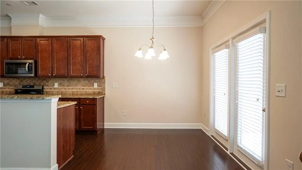 Kitchen with light stone countertops, a chandelier, stainless steel appliances, dark wood-style flooring, and decorative backsplash