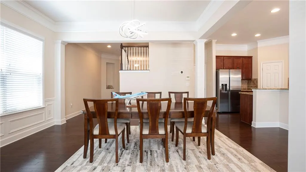 Dining area featuring crown molding, dark wood-style floors, a chandelier, and decorative columns